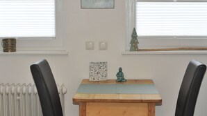 A dining area with a wooden table and two black chairs. There is a radiator on the left, a small decorative tree on the right, and a framed sign above the table. - Quiet, cozy vacation apartment near the forest. (Neustadt an der Weinstraße)
