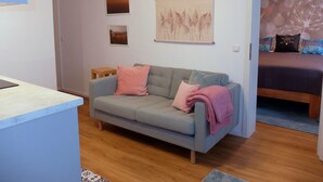 A modern living room with a grey sofa, a small wooden table, and a bed with patterned bedding. - Quiet, cozy vacation apartment near the forest. (Neustadt an der Weinstraße)