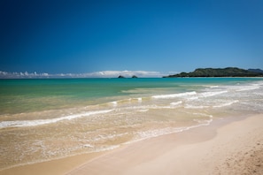 Een strand met helder turquoise water, zachte golven en heuvels in de verte.