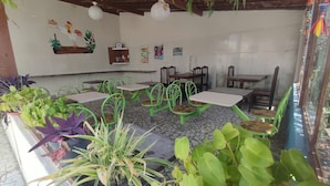 Un restaurante con sillas y mesas de metal verde, plantas en macetas y piso de baldosas.
