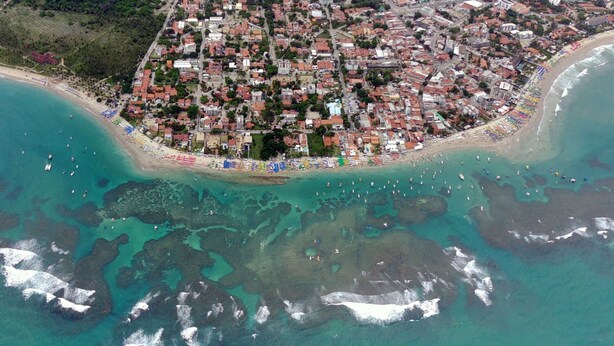 Vista aérea de un pueblo costero con playa bordeada por sombrillas y barcos.