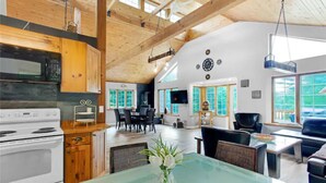 A spacious living area with a large glass table, wooden ceiling beams, and a dining area with chairs and a TV.
