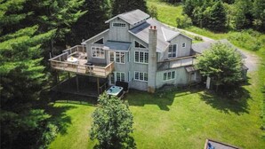 A large, two-story house with a deck and hot tub, surrounded by dense forest.