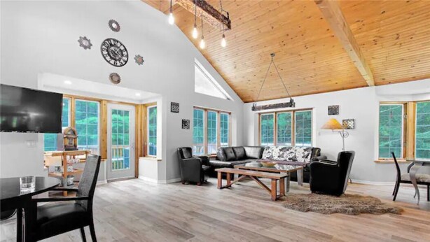 A spacious living room with a high wooden ceiling, large windows, and a modern fireplace.
