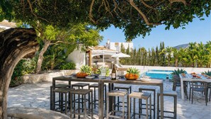 Un espace de restauration en plein air doté d’un sol en pierre, de tables et de chaises en bois, entouré de verdure et d’une piscine.