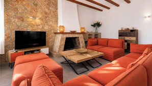 Un salon avec un mur en pierre, une cheminée, un téléviseur, des meubles orange et une table basse en bois.