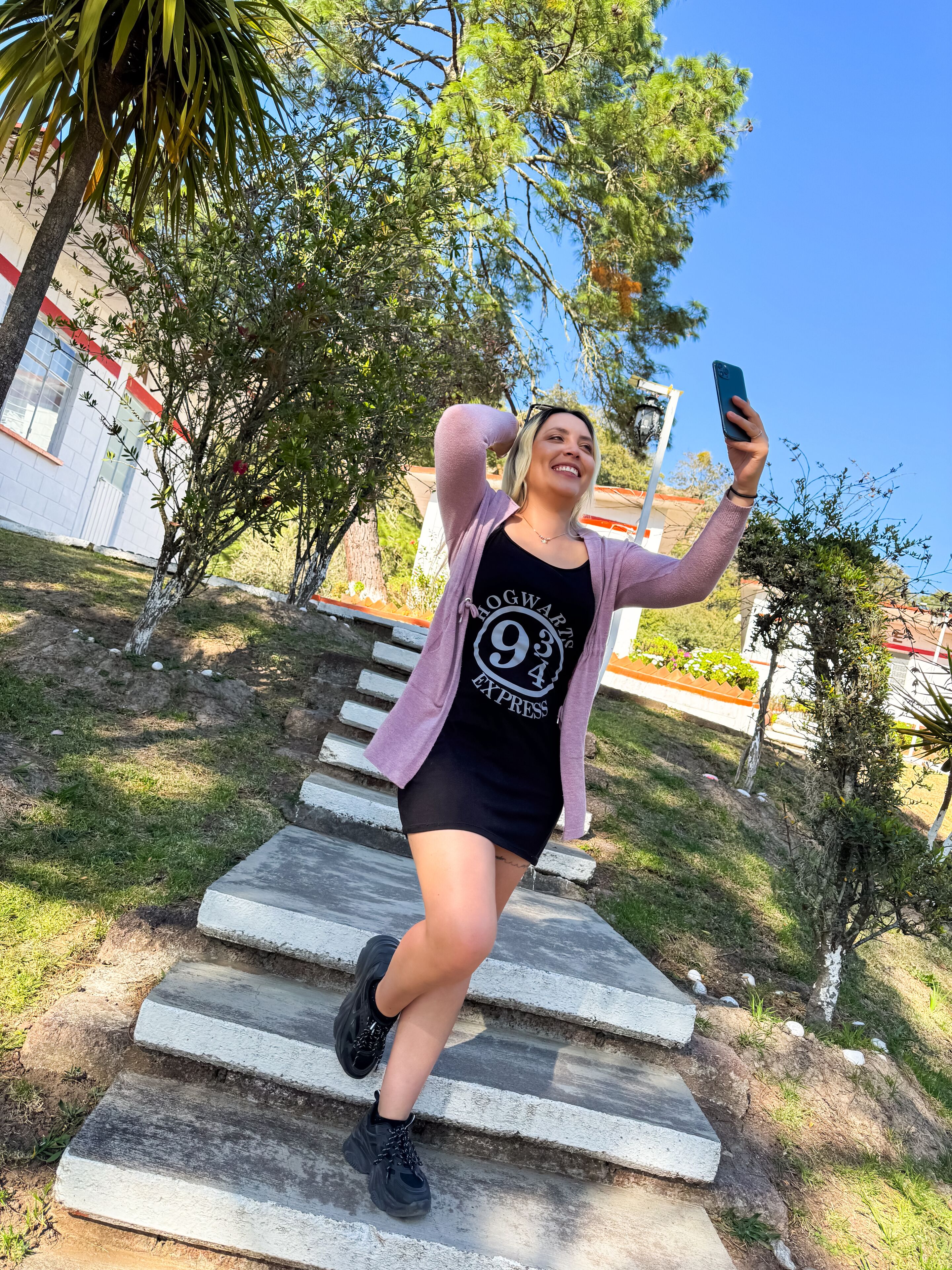 A person taking a selfie on outdoor steps with a building in the background.
