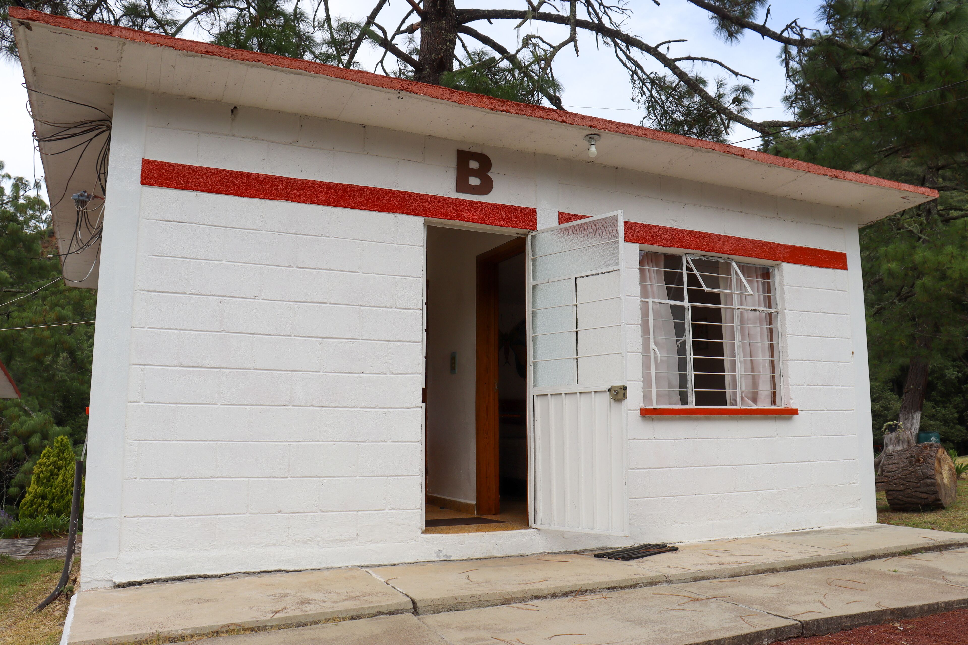 Un edificio pequeño de un piso con una franja roja y un letrero con la letra 'B' sobre la puerta.