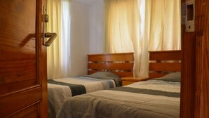Una habitación con dos camas de madera, una puerta de madera y cortinas.