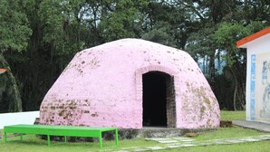 Una estructura en forma de cúpula rosa con una entrada, un banco verde al frente y un mural a la derecha.
