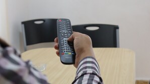Una persona sosteniendo un control remoto frente a un televisor instalado en la pared.