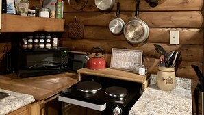 Una cocina con paredes de madera, estufa, microondas y varias ollas y sartenes colgadas en la pared.