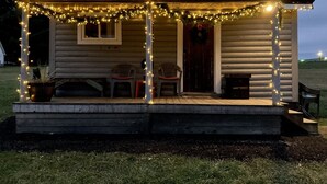 Una cabaña pequeña con un porche decorado con luces colgantes, un banco de madera y una puerta adornada con un adorno.