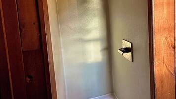 A small, enclosed shower area with a showerhead mounted on the wall, a drain in the floor, and wooden paneling on the ceiling.