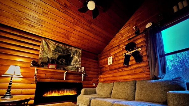 Interior acogedor de una cabaña con paredes de madera, una chimenea, un sofá y una lámpara.