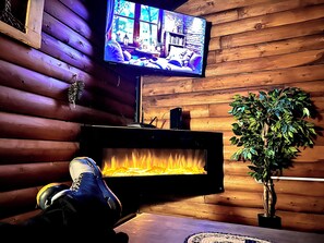 Una habitació acollidora amb una llar de foc, un televisor penjat a la paret i una planta en test.