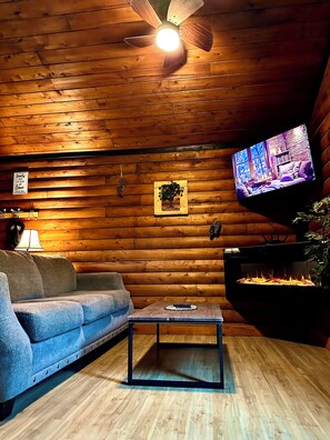 Una habitación acogedora con techo de madera, televisor montado en la pared, sofá, mesa de centro y chimenea.