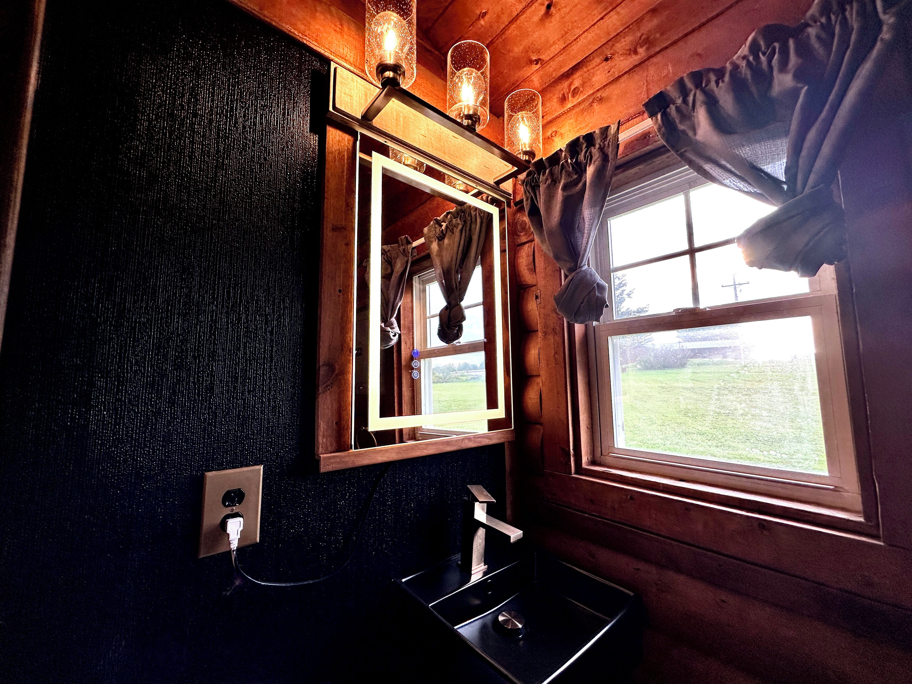 A bathroom with a wooden interior, a mirror, a sink, and a window with curtains.