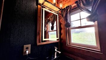 A bathroom with a wooden interior, a mirror, a sink, and a window with curtains.