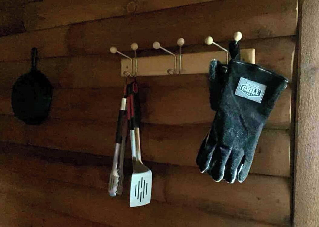 Cuina amb parets de fusta, una olla penjant, una espàtula i un parell de gants de forni.
