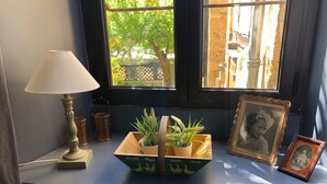 Seient a la finestra amb una làmpada, una jardiniera de fusta amb plantes, una fotografia emmarcada i una petita caixa de fusta amb ànecs.