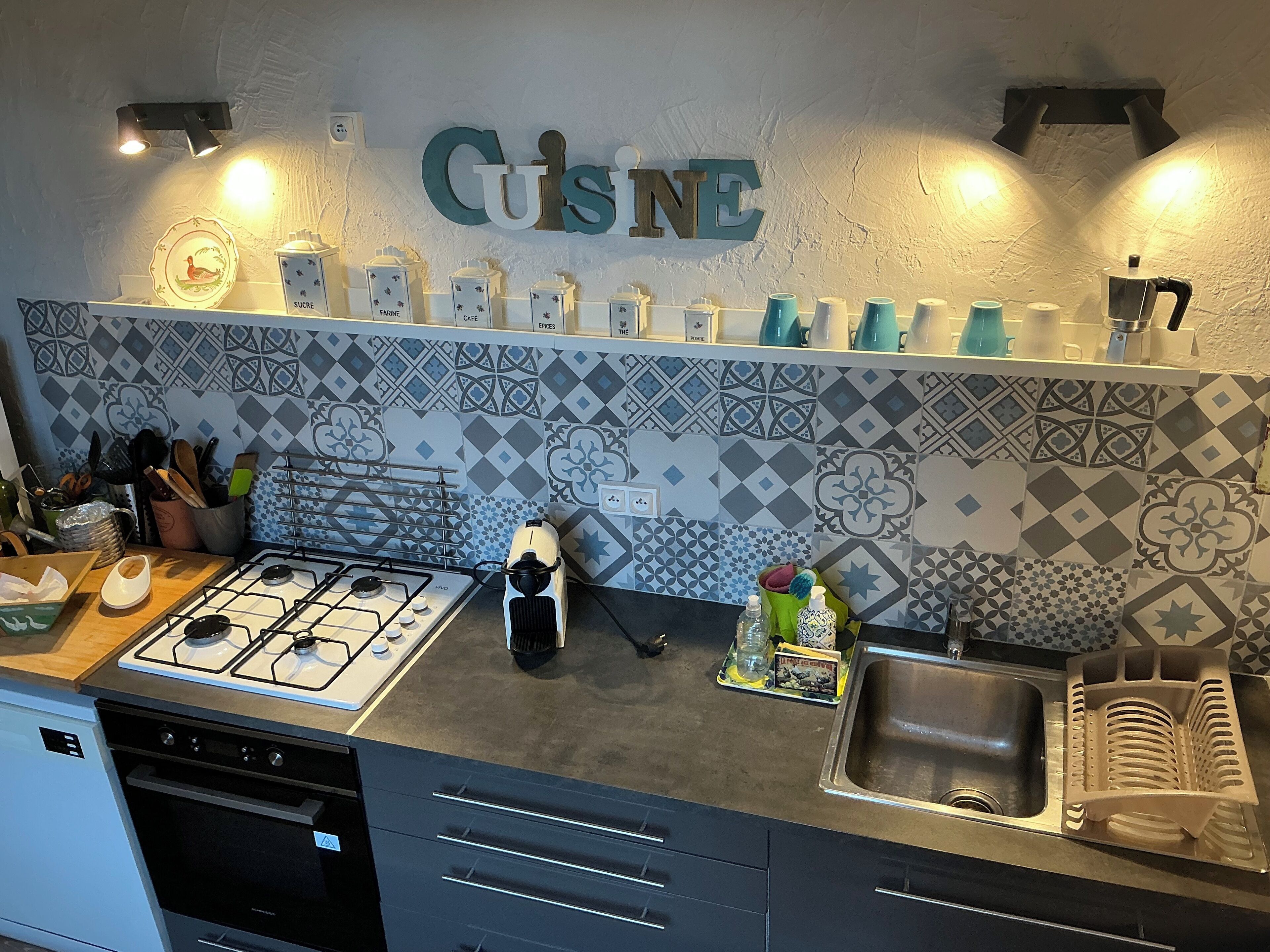Een keuken met een gasfornuis, een vaatwasser, een spoelbak en een spatwand met geometrische patronen.