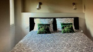 A bed with a geometric patterned bedspread, two pillows with a leafy design, and two wall-mounted lamps. - Auberge Sainte Marguerite - "Anse Méjean" room (La Garde)