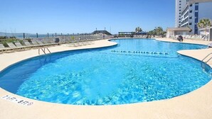 Un espace piscine avec une piscine à l’eau d’un bleu limpide, un poste de surveillance pour les sauveteurs et, en arrière-plan, un immeuble de grande hauteur.