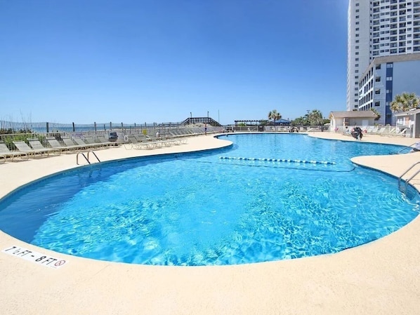 Un espace piscine avec une piscine à l’eau d’un bleu limpide, un poste de surveillance pour les sauveteurs et, en arrière-plan, un immeuble de grande hauteur.