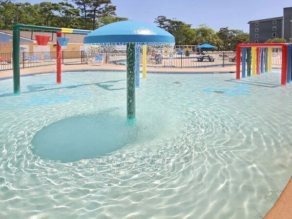 Piscina cristalina com um elemento central de água e estruturas lúdicas ao redor.