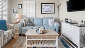 Un salon avec un canapé bleu clair, une table basse en bois, un meuble blanc et un téléviseur fixé au mur.