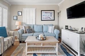 Un salon avec un canapé bleu clair, une table basse en bois, un meuble blanc et un téléviseur fixé au mur.