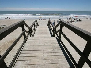 Une promenade en bois menant à une plage où se trouvent des gens et des parasols.