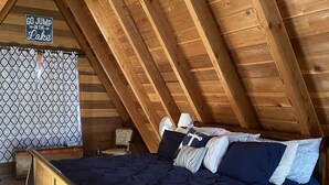 Une chambre avec un plafond en bois, un lit avec une literie bleue et une pancarte sur laquelle on peut lire : « ALLEZ, SAUTEZ DANS LE LAC ! »