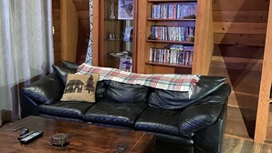 L’intérieur chaleureux d’un chalet en bois comprend un canapé en cuir, une table basse en bois et une bibliothèque remplie de livres.