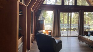 L’intérieur d’une cabane avec une grande fenêtre, des murs en bois, un fauteuil en cuir et une pancarte sur laquelle on peut lire : « Je préférerais me perdre au bord du lac plutôt que de me retrouver chez moi. »