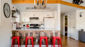 Una cocina con armarios blancos, una isla de madera con taburetes rojos y un reloj en la pared.