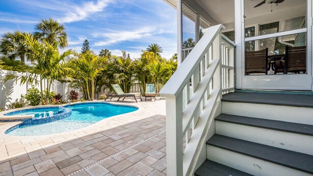 A swimming pool with a tiled edge, surrounded by palm trees and a white fence. - Royal Palm: Pool, 2 Blocks to Beach, Close to Dining & Shopping by Anna Maria Life Vacation Rentals (Holmes Beach)