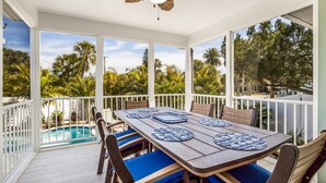 A covered outdoor dining area with a pool, wooden table, blue cushions, and a ceiling fan. - Royal Palm: Pool, 2 Blocks to Beach, Close to Dining & Shopping by Anna Maria Life Vacation Rentals (Holmes Beach)