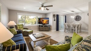 A modern living room with a television, comfortable seating, a dining area, and a ceiling fan. - Royal Palm: Pool, 2 Blocks to Beach, Close to Dining & Shopping by Anna Maria Life Vacation Rentals (Holmes Beach)