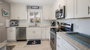 A modern kitchen with white cabinets, stainless steel appliances, and a sign reading "BEACH HOUSE". - Royal Palm: Pool, 2 Blocks to Beach, Close to Dining & Shopping by Anna Maria Life Vacation Rentals (Holmes Beach)
