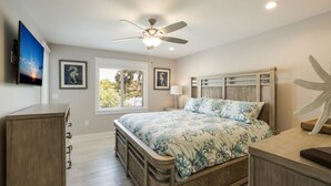 A bedroom with a bed, a ceiling fan, a window with blinds, a TV, and a wooden dresser. - Royal Palm: Pool, 2 Blocks to Beach, Close to Dining & Shopping by Anna Maria Life Vacation Rentals (Holmes Beach)