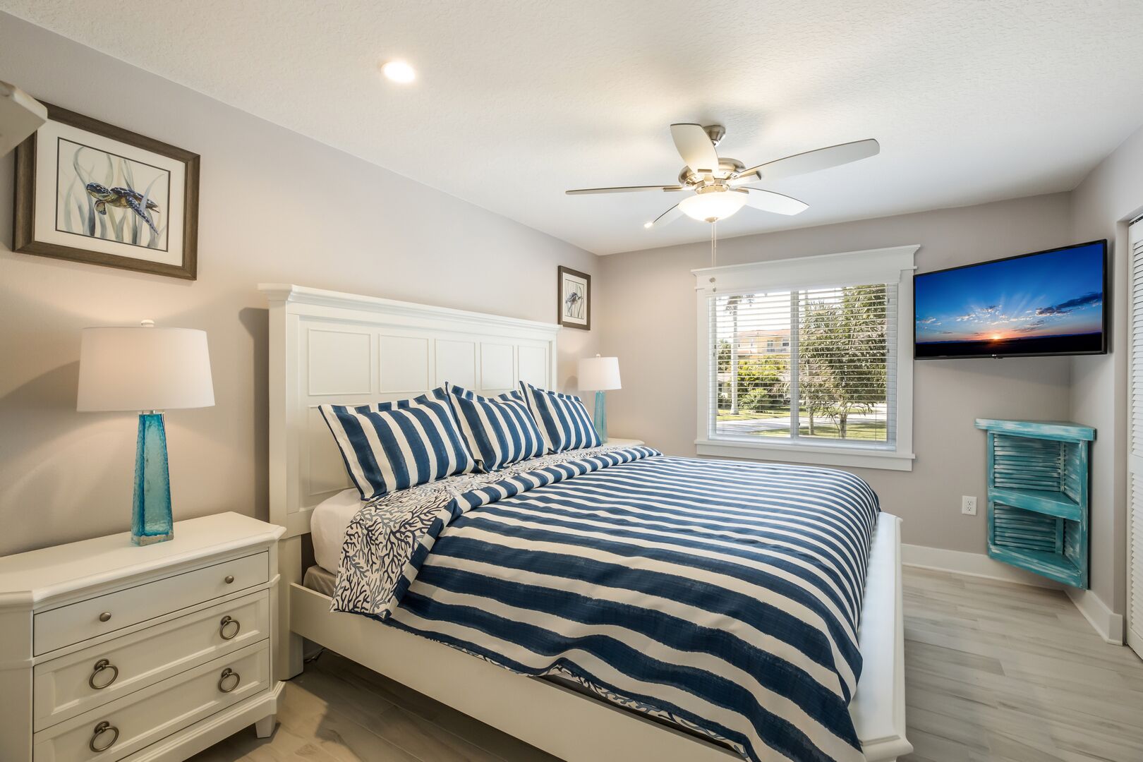 A bedroom with a bed, nightstands, a TV, and a ceiling fan.