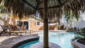 A pool area with lounge chairs and a thatched roof structure. - Tiki Cottage: 2.5 Blocks to Beach, Pool with Swim up Tiki Bar by Anna Maria Live Vacation Rentals (Holmes Beach)