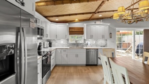 A modern kitchen with stainless steel appliances, white cabinetry, and a wooden ceiling. - Tiki Cottage: 2.5 Blocks to Beach, Pool with Swim up Tiki Bar by Anna Maria Live Vacation Rentals (Holmes Beach)