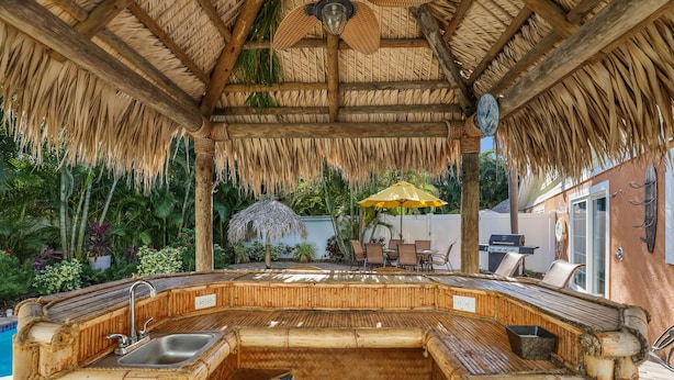A thatched-roof outdoor kitchen with a built-in grill and seating area. - Tiki Cottage: 2.5 Blocks to Beach, Pool with Swim up Tiki Bar by Anna Maria Live Vacation Rentals (Holmes Beach)