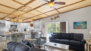 A modern living room with a dark grey sofa, matching armchairs, and a dining area with a white table and chairs. - Tiki Cottage: 2.5 Blocks to Beach, Pool with Swim up Tiki Bar by Anna Maria Live Vacation Rentals (Holmes Beach)