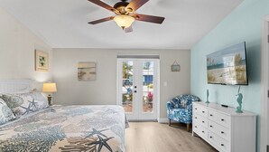 A bedroom with a bed, a ceiling fan, a dresser, and a TV. - Tiki Cottage: 2.5 Blocks to Beach, Pool with Swim up Tiki Bar by Anna Maria Live Vacation Rentals (Holmes Beach)