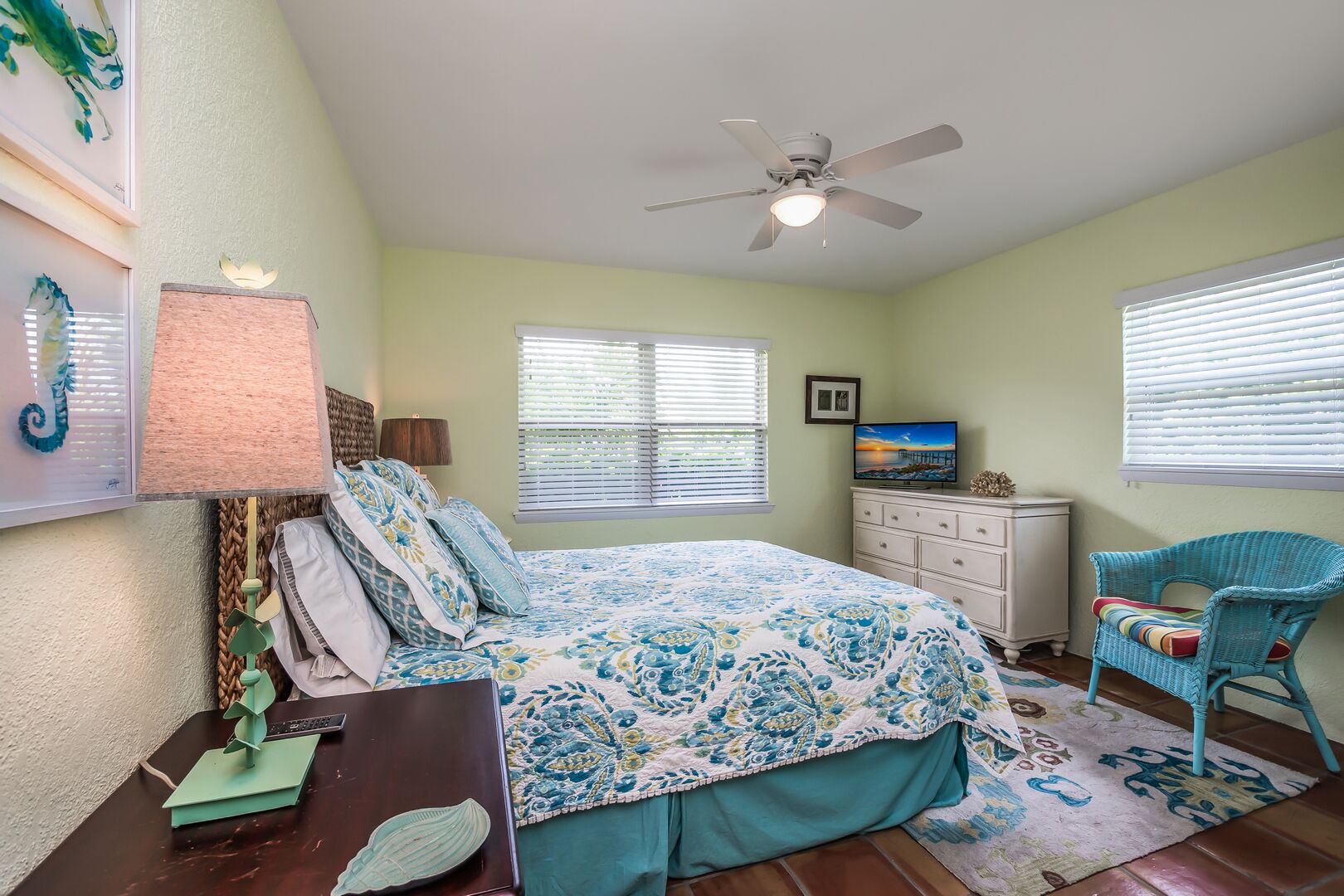A bedroom with a bed, a desk, a chair, a television, and a ceiling fan.