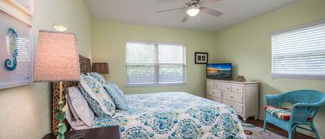A bedroom with a bed, a desk, a chair, a television, and a ceiling fan.